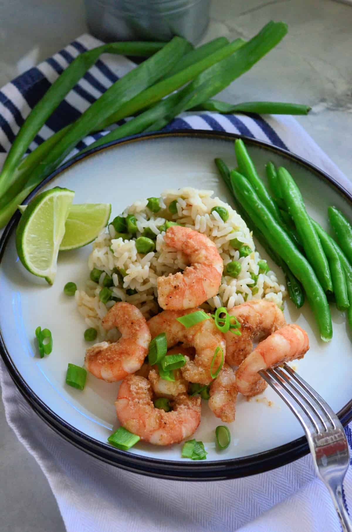 Assiette blanche remplie de riz blanc, de pois et de crevettes avec une fourchette piquant un morceau de crevette.