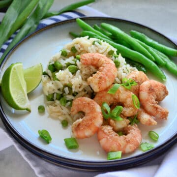 Assiette ronde blanche avec crevettes, riz, oignons verts et haricots verts sur une assiette posée sur un torchon.