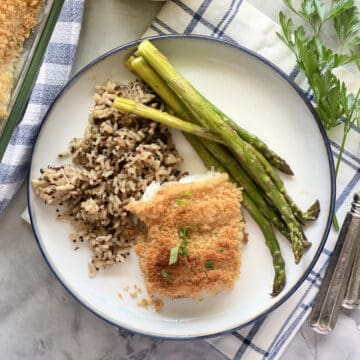 Vue de dessus d'un morceau de poisson pané sur une assiette blanche remplie de riz sauvage et d'asperges.