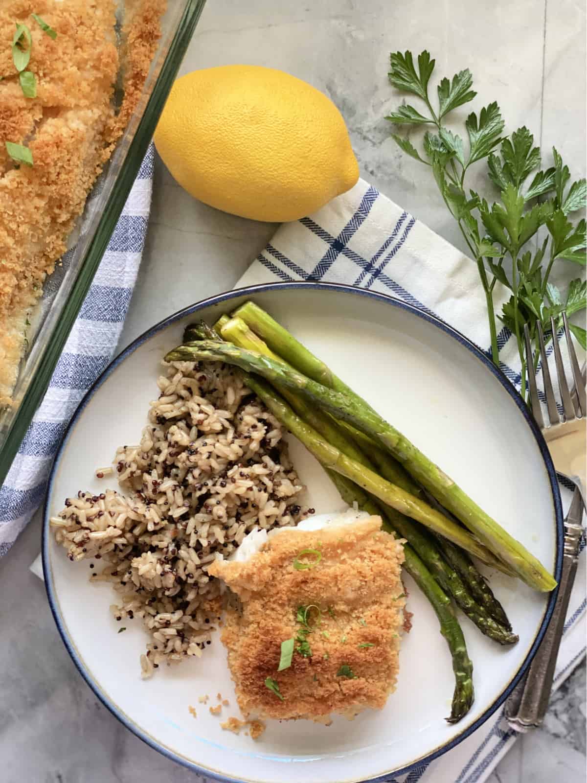 Vue de dessus d'une assiette blanche avec du poisson pané, des asperges et du riz sauvage.