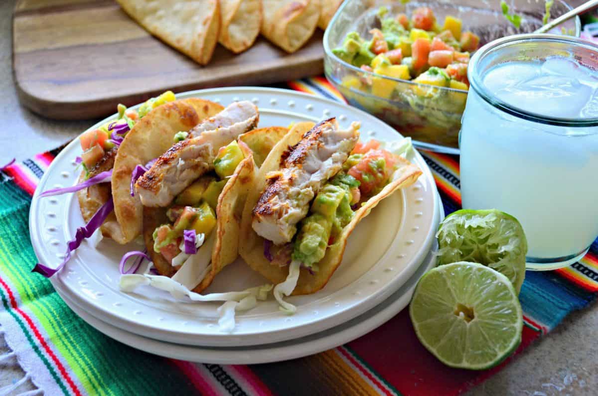 3 tacos au poisson Mahi Mahi plaqués avec salsa à la mangue et à l'avocat, accompagnés de citron vert et d'une boisson glacée jaune.