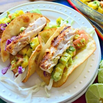 Assiette ronde blanche avec trois tacos au poisson moelleux avec avocat et chou dessus.