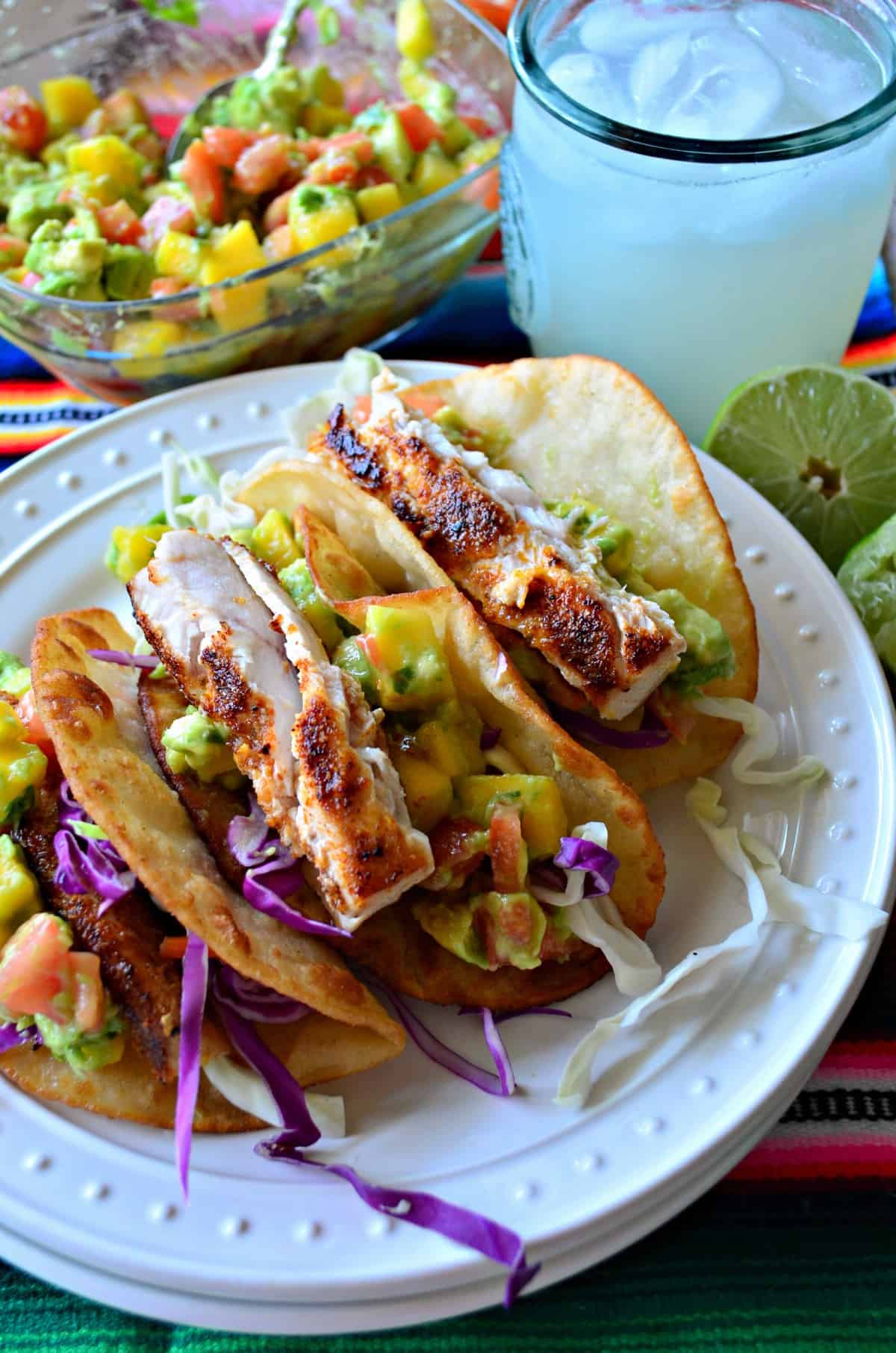 gros plan Tacos au poisson avec salsa à la mangue et à l'avocat avec une margarita et une salsa à la mangue et à l'avocat en arrière-plan.