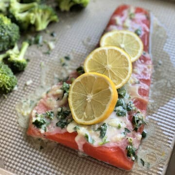 Gros morceau de saumon cru avec trois tranches de citron, du beurre et des herbes sur une plaque à pâtisserie.