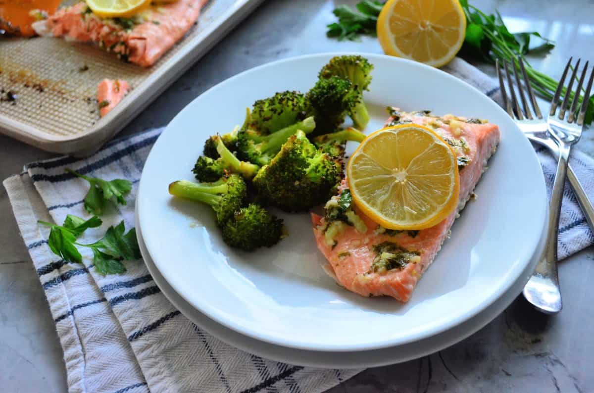 Assiette de saumon cuit garnie d'une rondelle de citron servie avec du brocoli rôti à côté des fourchettes.