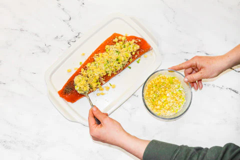 Filet de saumon sur un plat blanc tandis que le chef Nicole verse le mélange de poireaux et d'ananas sur le saumon.