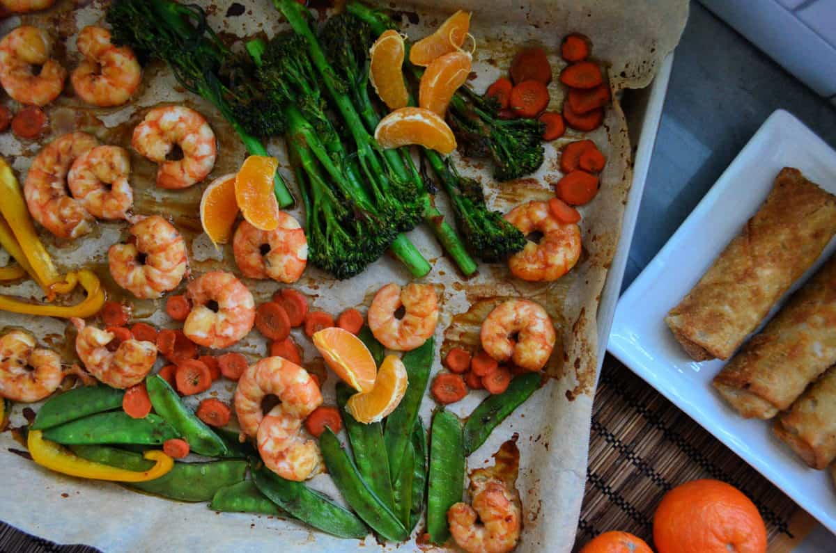 pois, brocolini, mandarines, crevettes, poivrons et carottes sur papier sur une plaque à pâtisserie.