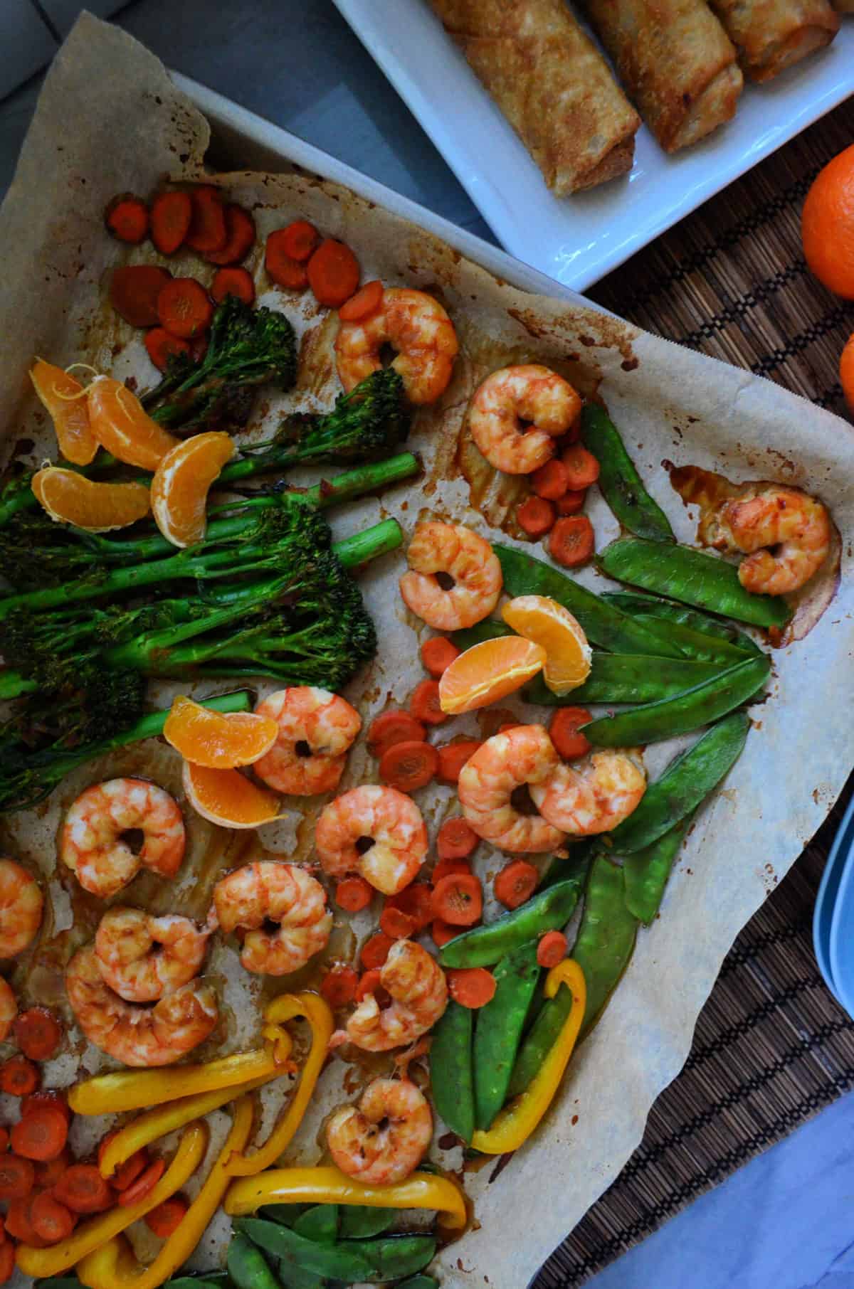 Gros pois, broccolini, oranges mandrines, crevettes, poivrons et carottes sur papier sur plaque à pâtisserie.