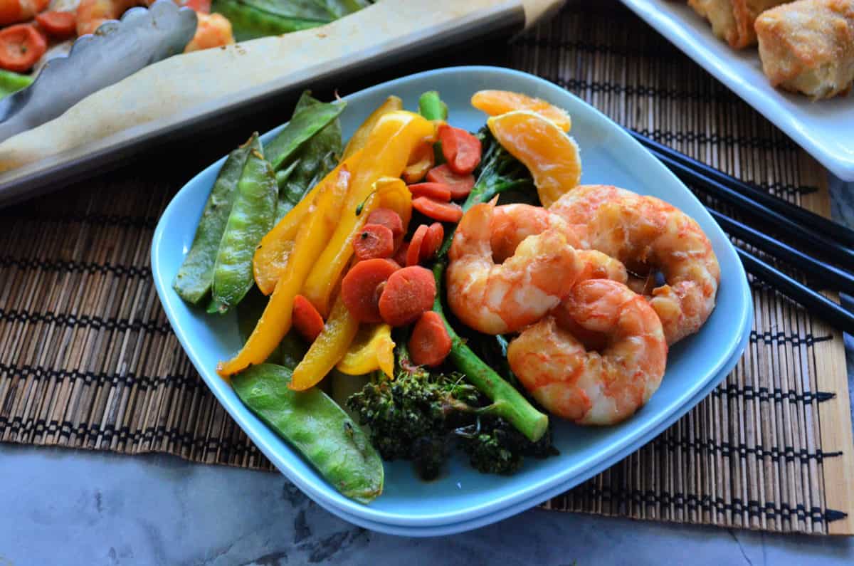 pois, broccolini, oranges mandarines, crevettes, poivrons et carottes sur papier sur assiette avec baguettes.