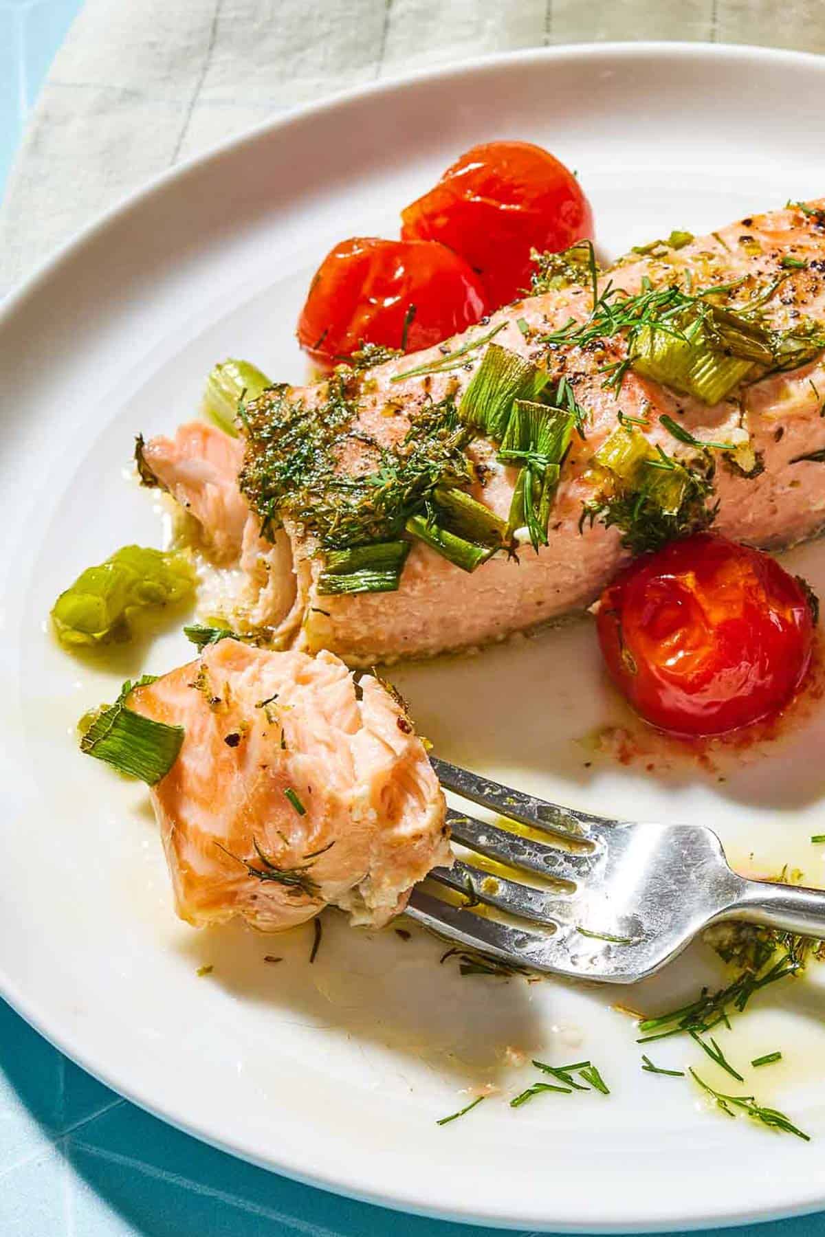 Un gros plan d'un filet de saumon grec sur une assiette avec une fourchette et quelques tomates cerises.