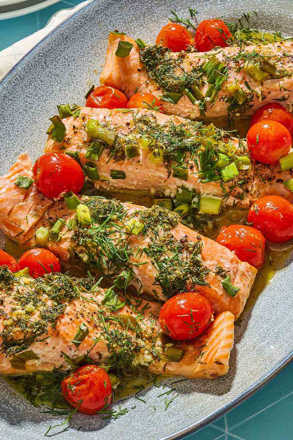 Un gros plan de 4 filets de saumon grec aux tomates cerises sur un plateau.