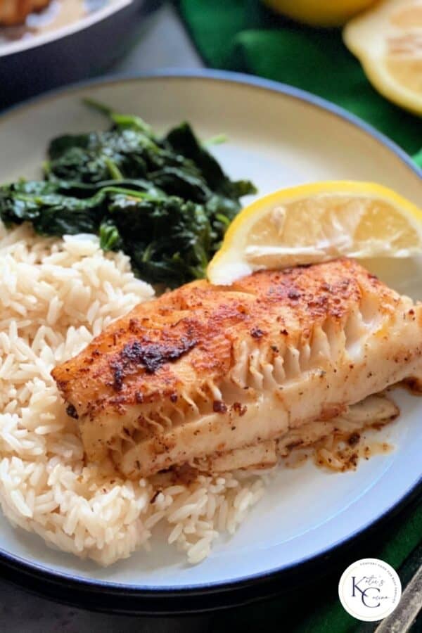Morue noircie, riz blanc, épinards et tranche de citron sur une assiette blanche