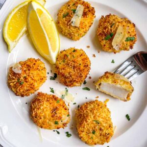 plate of crunchy, coated air fryer sea scallops with panko and parmesan, garnished with two lemon wedges.