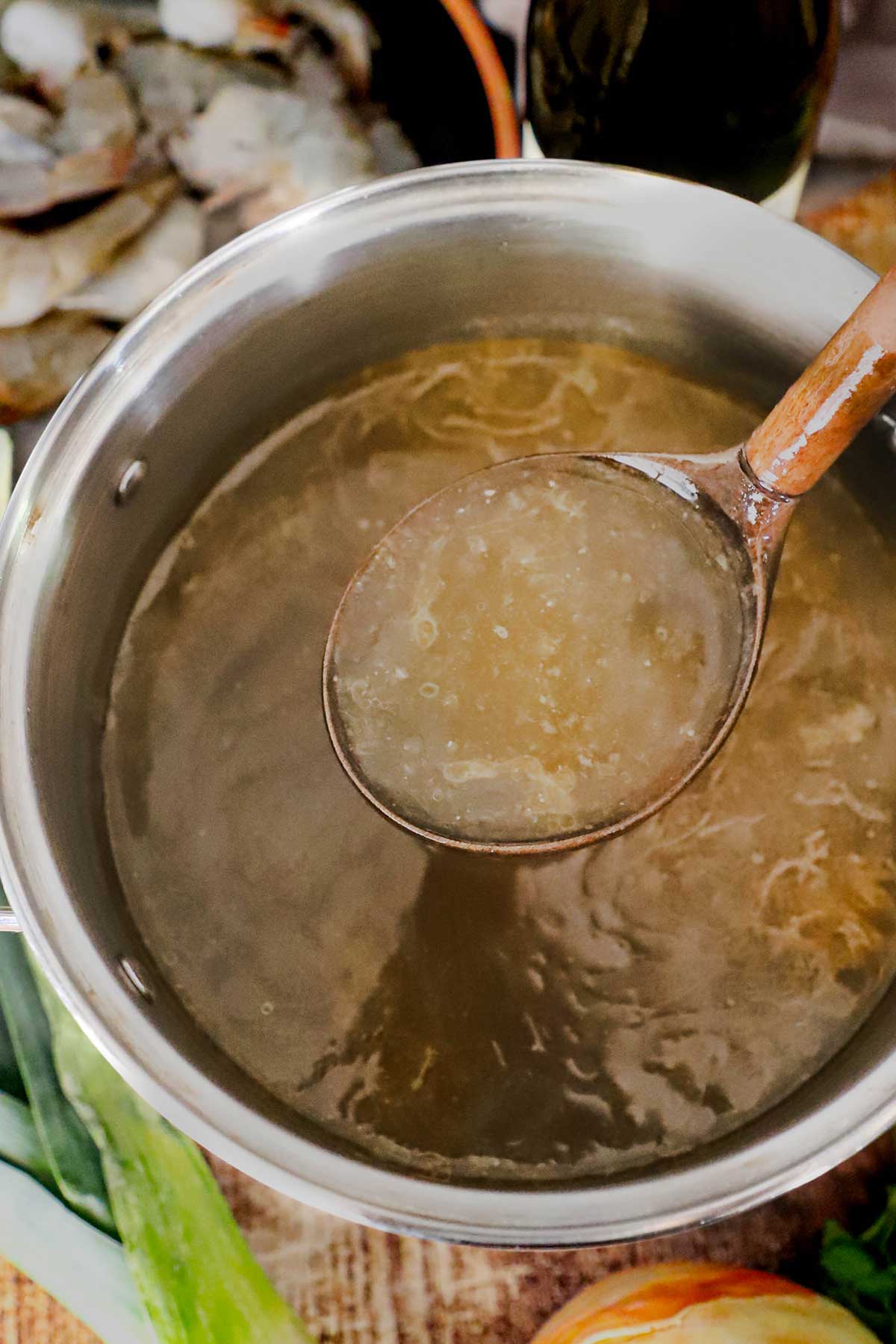 Une personne utilisant une grande louche en bois pour lever une louche de bouillon de crustacés fait maison à partir d'une marmite remplie de bouillon.