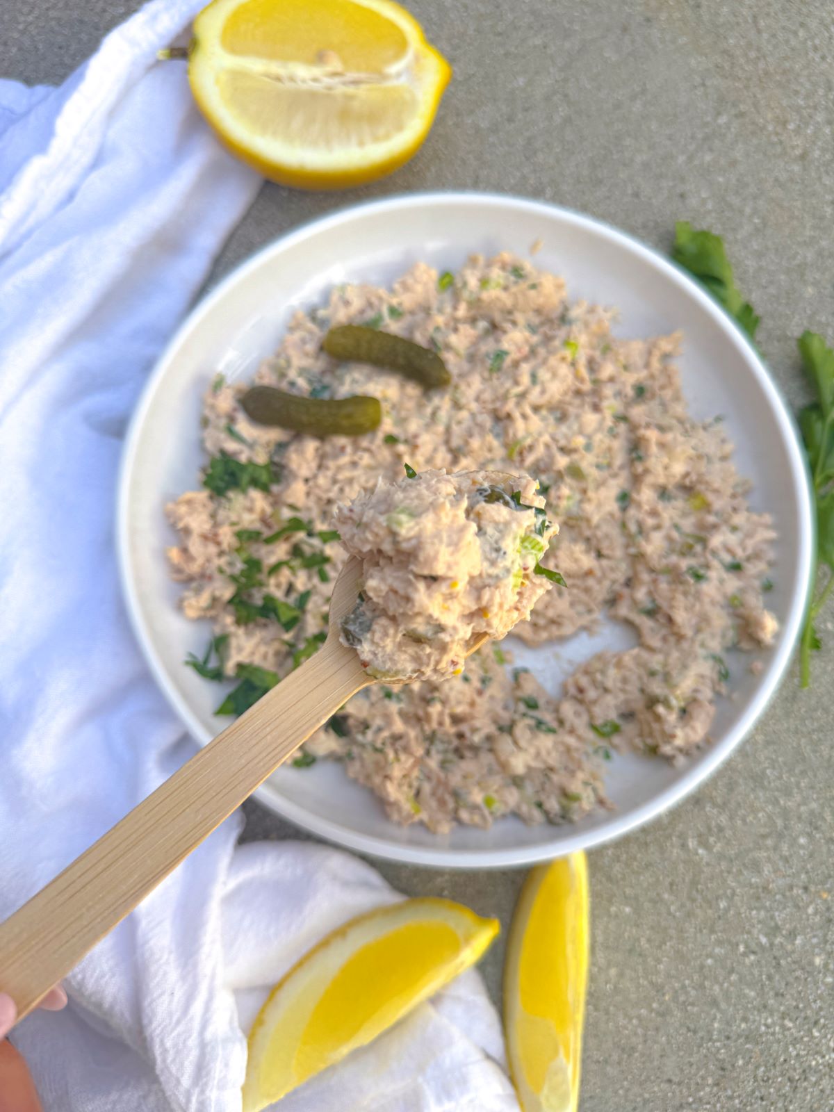 salade de saumon en conserve sur une cuillère levée sur l'assiette de la recette et tranches de citron à proximité