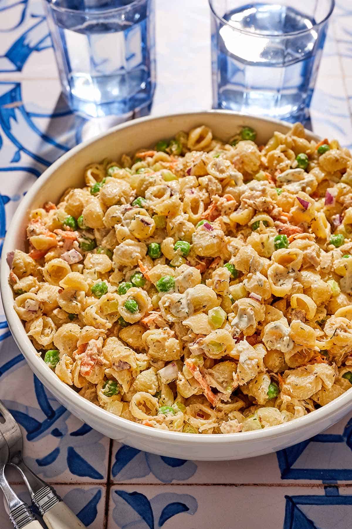 Salade de pâtes au thon dans un bol de service à côté de deux verres d'eau.