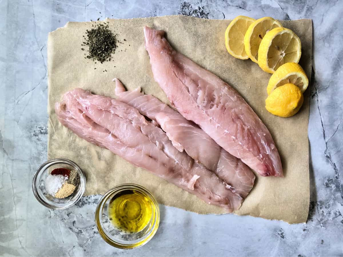 Deux grosses tranches de vivaneau sur papier sulfurisé avec des épices dans un bol en verre, du citron et de l'huile d'olive.