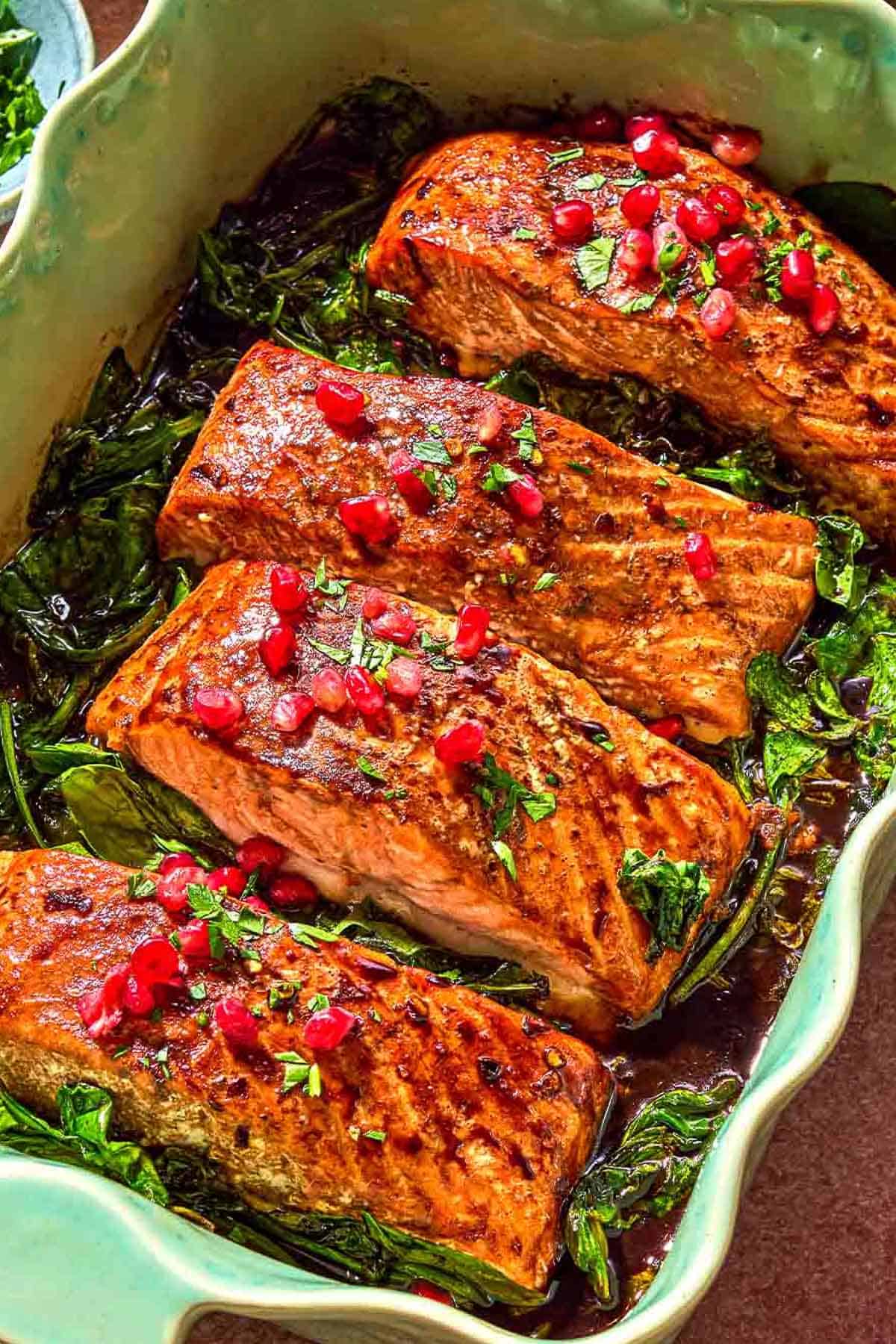 Filets de saumon glacés garnis d'arilles de grenade sur un lit de pousses d'épinards dans un plat allant au four.