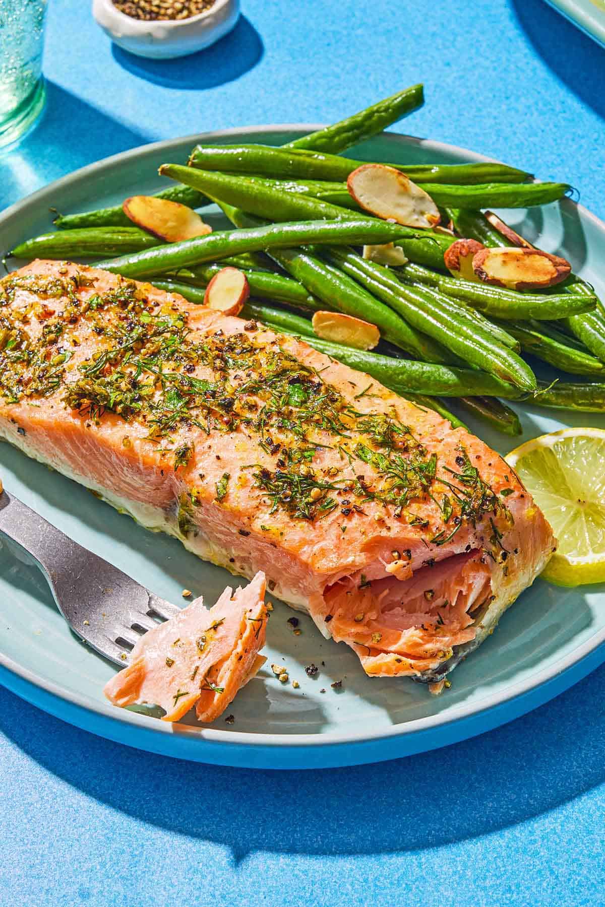 Un filet de saumon au poivre citronné sur une assiette avec des haricots verts rôtis, une meule de citron et une fourchette contenant un peu de saumon.
