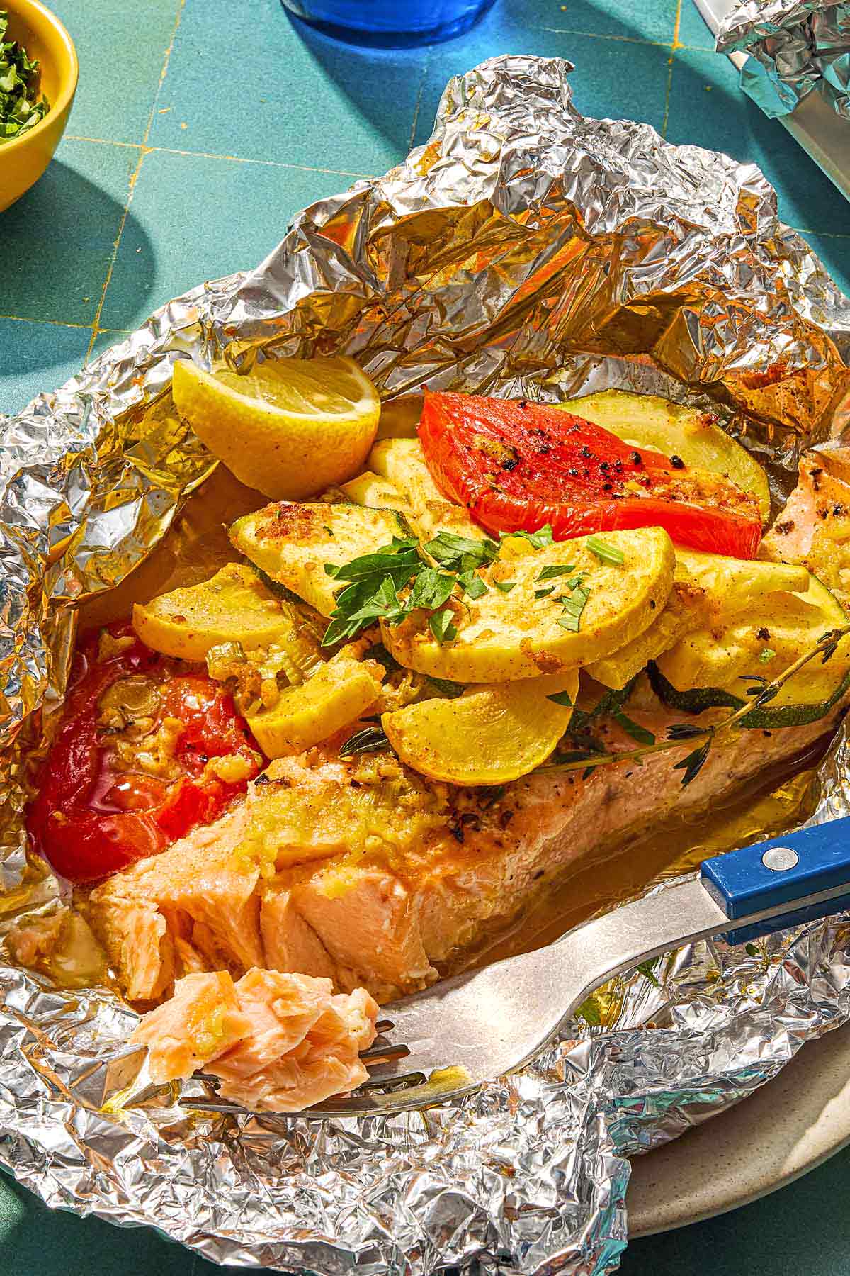 Une portion de saumon cuit au four ouvert en papillote avec des légumes sur une assiette avec une fourchette.