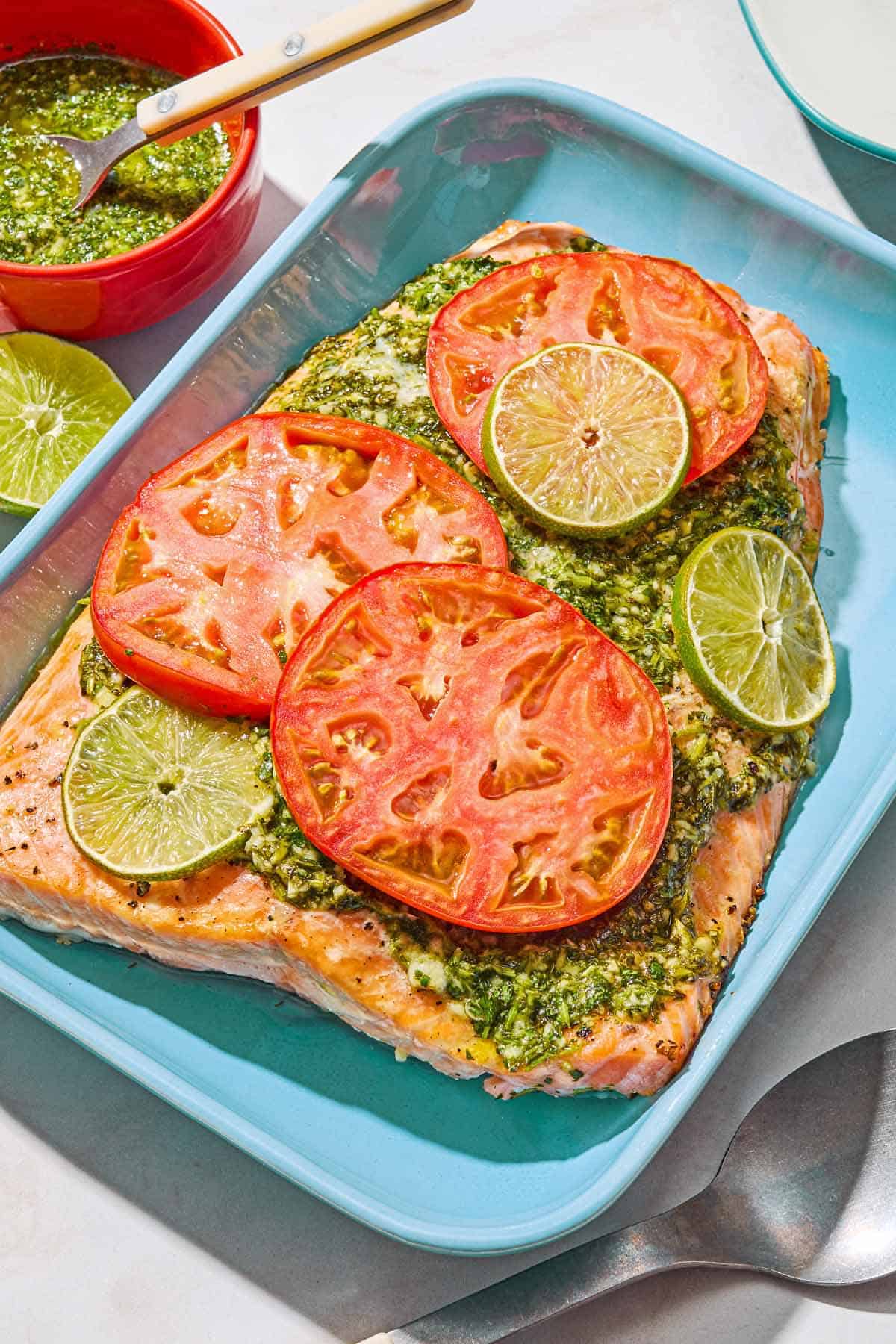 Saumon à la coriandre et au citron vert non cuit dans un plat allant au four. À côté se trouvent une cuillère de service, un bol de sauce à la coriandre et un demi citron vert.