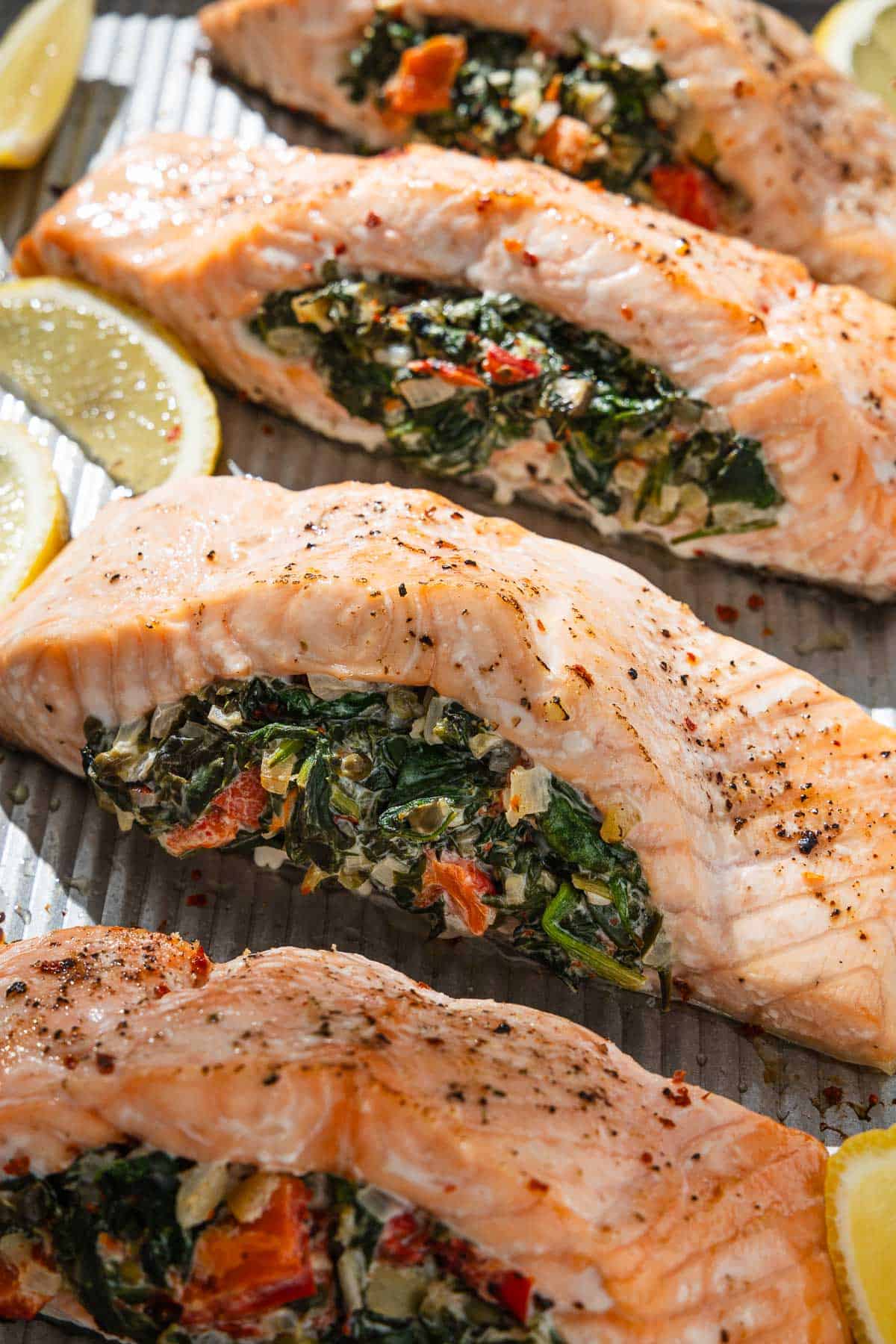 Un gros plan de 4 filets de saumon farcis cuits sur une plaque à pâtisserie avec des quartiers de citron.