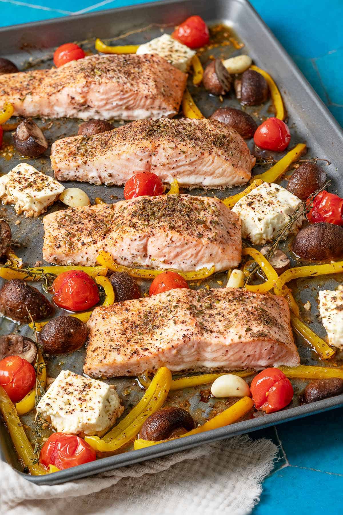 cuire des filets de saumon cuits au four avec des légumes et de la feta sur une plaque posée sur une serviette en lin blanc.