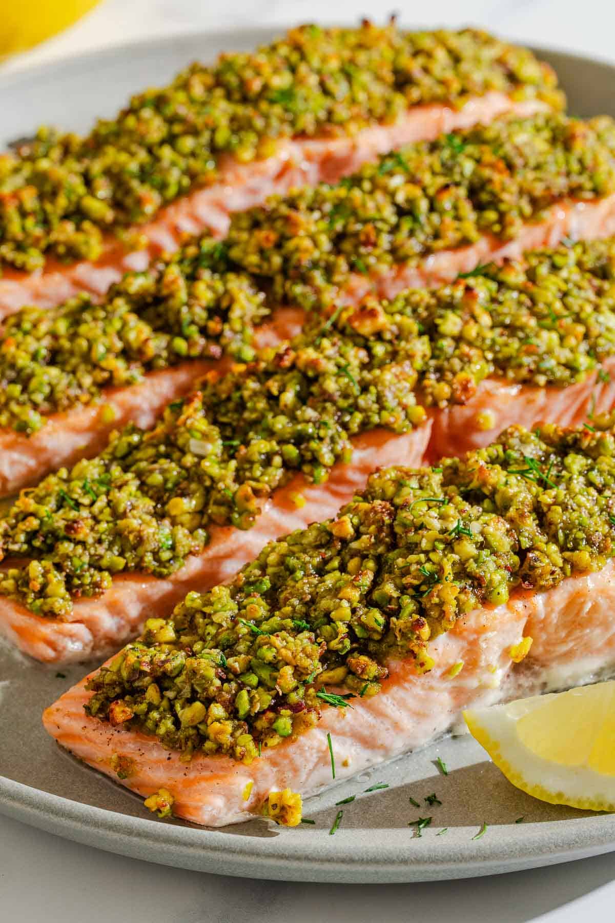 Quatre filets de saumon en croûte de pistaches sur une assiette avec des quartiers de citron.